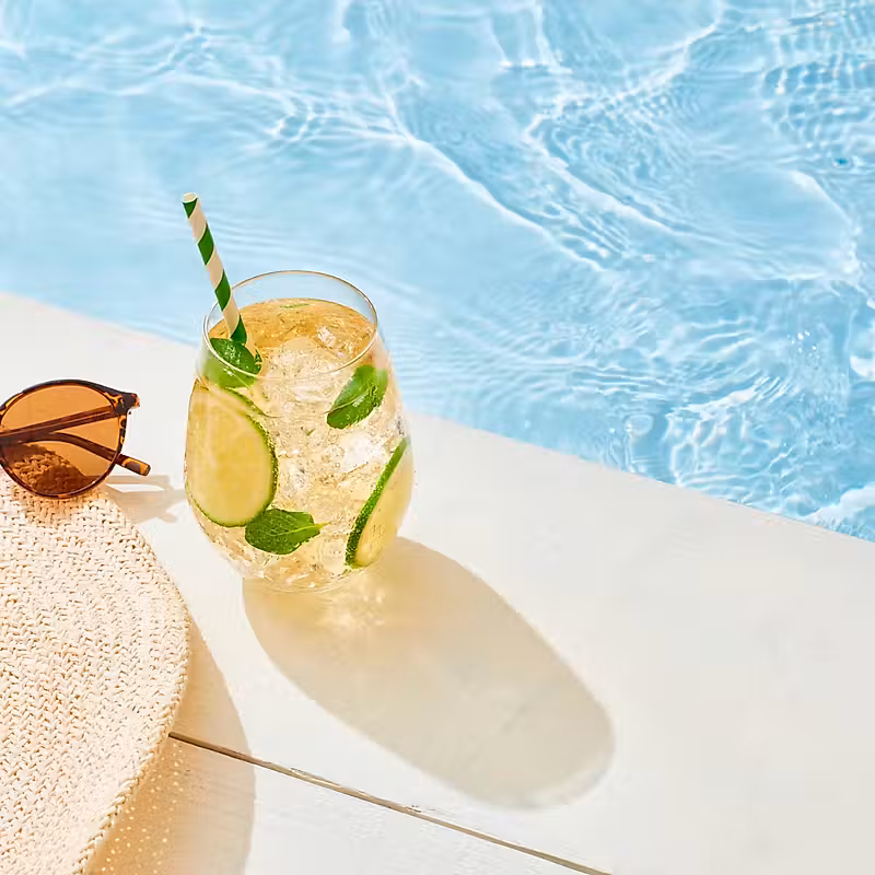 un chapeau, des lunettes de soleil et une boisson au bord de la piscine