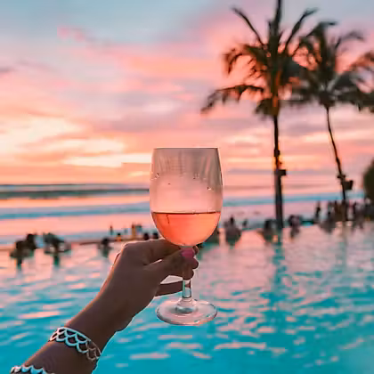 Une main tenant un verre de vin devant la piscine au coucher du soleil à Bali, en Indonésie.