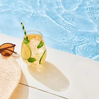 un chapeau, des lunettes de soleil et une boisson au bord de la piscine