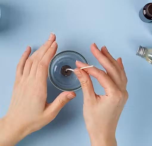 Mains fixant une mèche dans un bocal à bougie transparent